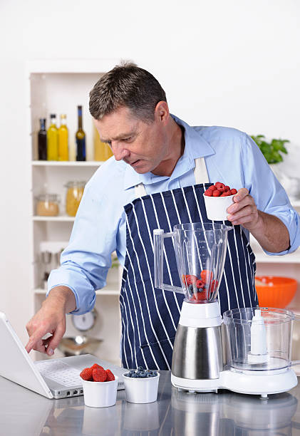 istock Mature Man Using Online Recipe To Make Healthy Drink/ dessert 184354071