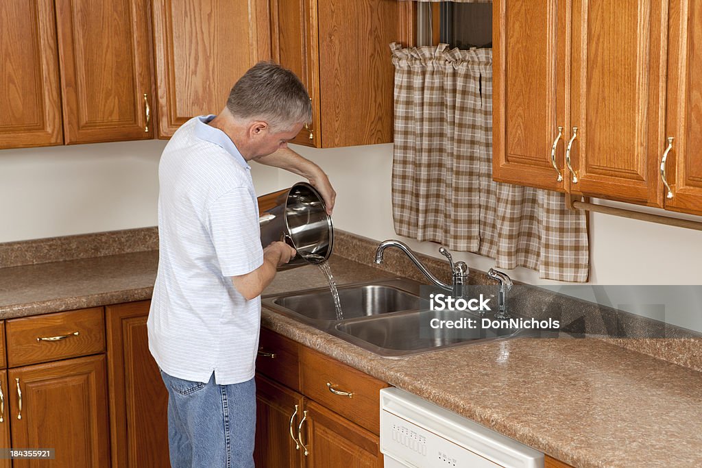 Uomo versare pentola d'acqua nel lavandino - Foto stock royalty-free di Lavare i piatti
