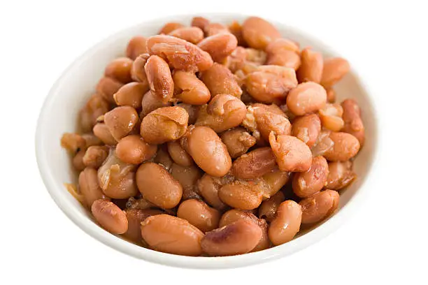A high angle close up of a small white bowl containing cooked Mexican style pinto beans.