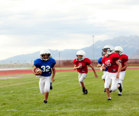 A young football player evades the defense as he runs down the sideline of a youth league football game.