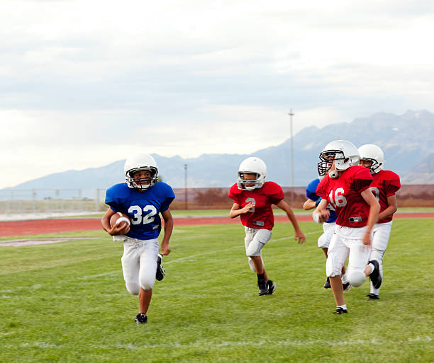 Touchdown Run A young football player evades the defense as he runs down the sideline of a youth league football game. american football field photos stock pictures, royalty-free photos & images