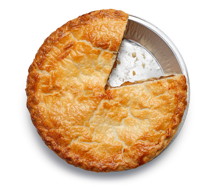 A top view of an apple pie with a slice removed on a white background.  The flaky, golden crust invites the viewer to reminisce.  The pie sits in a foil tin with one slice taken out leaving behind traces of the pie.  Pie filling just barely oozes out of the edges, leaving one to wonder who took the slice?