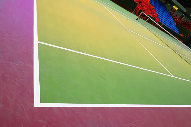 Professional hard court surface tennis court. Dark background. Spectator seats in the background.