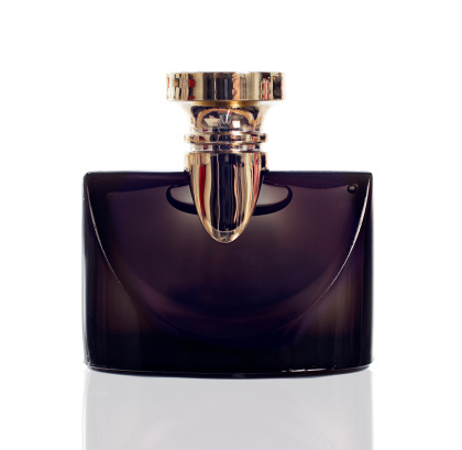 An elegant fragrance bottle made from black glass with a gold lid and fittings, against white.