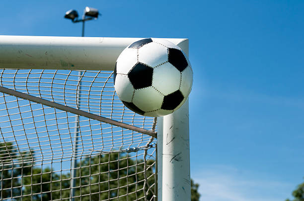 Soccer ball flys high in the air. Maybe it will make a great goal or the ball will hit the post.