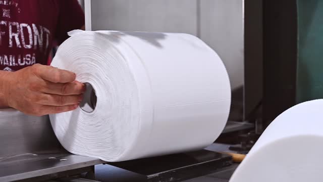 A toilet paper factory worker cuts a large roll of paper into rolls of paper towels. Greek manufacture of paper rolls for hygiene. Close up view. Selective focus. Slow motion
