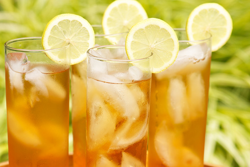 Tray of four glasses of refreshing iced tea garnished with lemon served outdoors