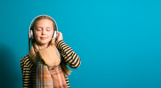 Girl 8-10 years old enjoying calm music with headphones, winter concept, banner, blue background