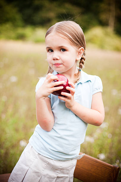 Young Girl holding a apple and smiling at camera while outdoors. Focus on Apple