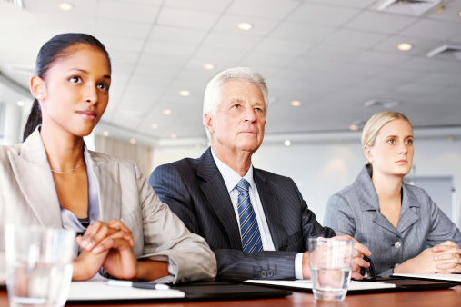 Three diverse business people sit at a conference table during a meeting. Horizontal shot.