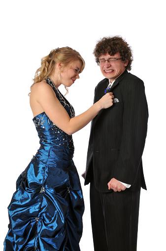 vertical image of teenage couple ready for the prom. she is pinning on his boutonniere and he is a bit nervous.