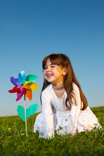 Happy little girl having fun with pinwheel outdoors.