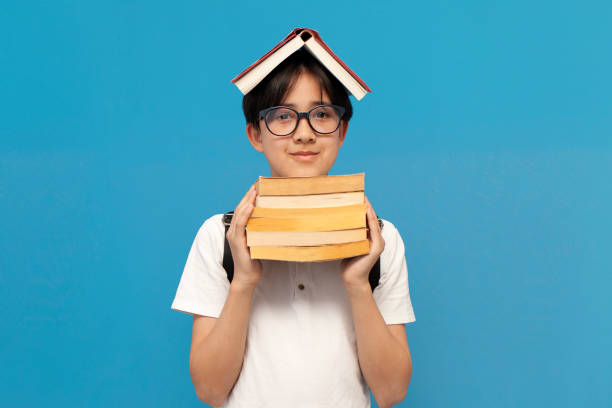 niño asiático escolar de doce años con gafas y con mochila sostiene muchos libros - 10 11 years little boys child happiness fotografías e imágenes de stock