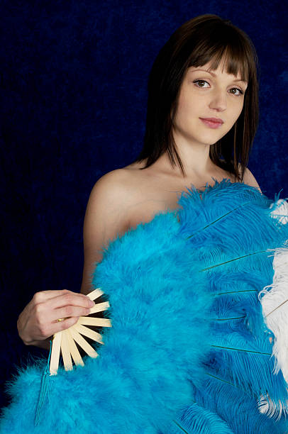 Beauty with blue feather fan. Beautiful young burlesque dancer with big blue and white fans.  Vertical studio shot on blue crushed velvet. ostrich feather stock pictures, royalty-free photos & images