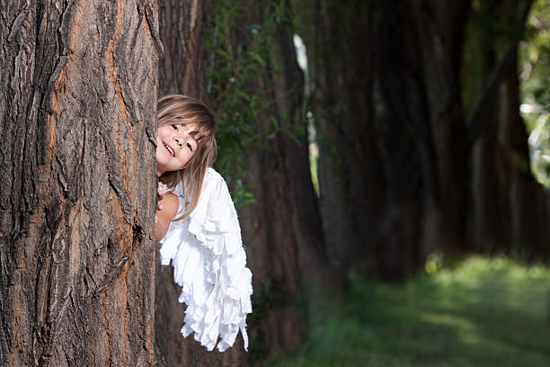 Angel with white wings on green grass. Brunette boy