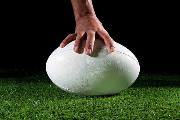 A hand holding down a white rugby ball in green AstroTurf.