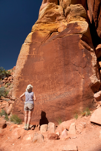 A young woman looks closely the ancient puebloan or Native American petroglyphs in the Paria Plateau in the Vermilion Cliffs National Monument of Arizona. Many patterns and designs are similar to Ancient Puebloan pottery designs nearly 1000 years ago.