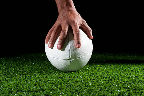 istock White rugby ball with hand holding it in grass 184371319