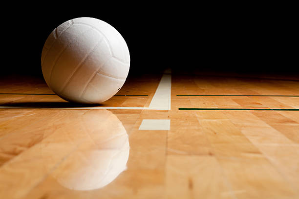 A volleyball and reflection on a wooden floor A white volleyball on the floor in a darkened gym. volleyball stock pictures, royalty-free photos & images