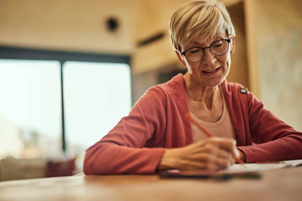 istock A happy grandma using a crayon and coloring the coloring book, at home. 1843728332