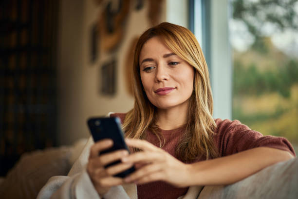 istock A woman using a mobile phone while sitting on the couch, smiling. 1843729389