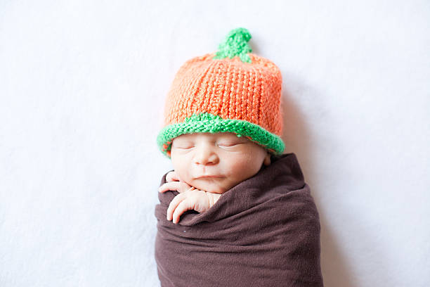 Newborn Baby Swaddled While Wearing a Pumpkin Hat stock photo