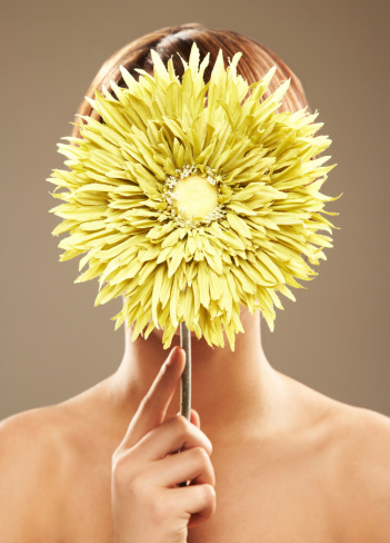 Close-up of a young beautiful woman naked covering her face with a green sun flower.  Vertical shot.