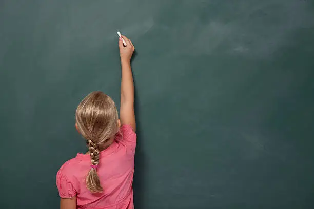 Photo of Back view Of Little Girl Writing On Blank Blackboard