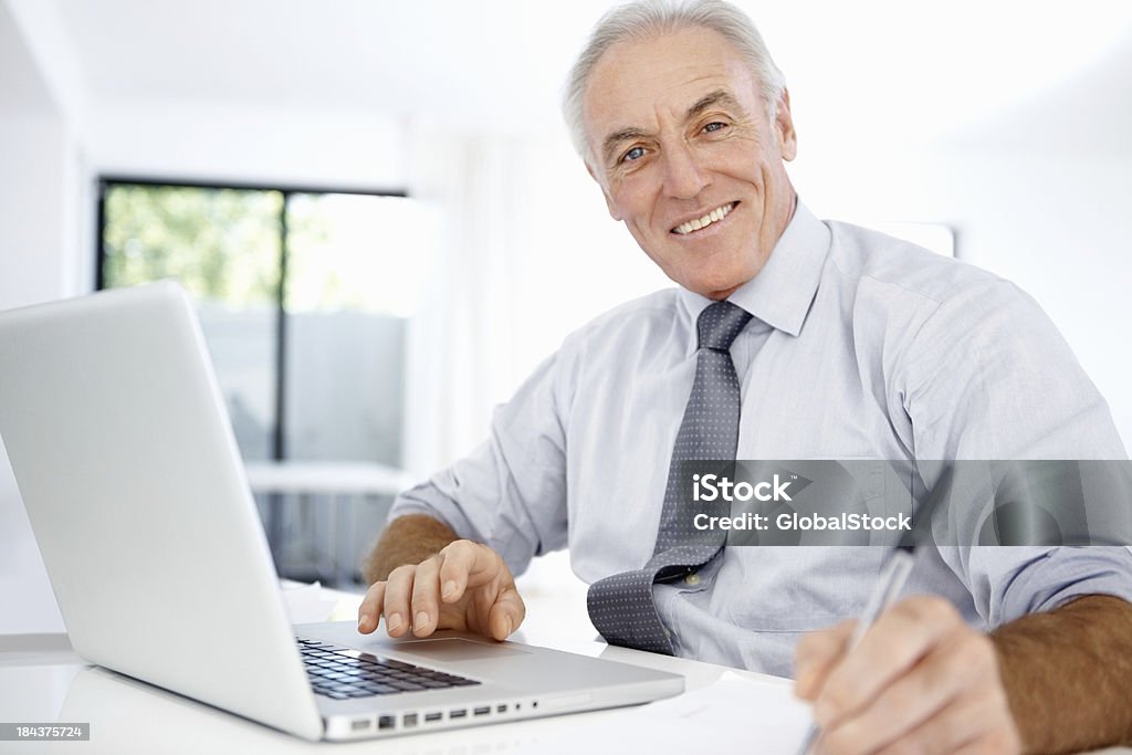 Homem de negócios usando o laptop e escrevendo em papel - Foto de stock de 60 Anos royalty-free