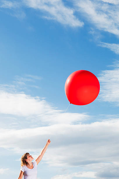 istock Young woman holding a red balloon under the sky 184376878