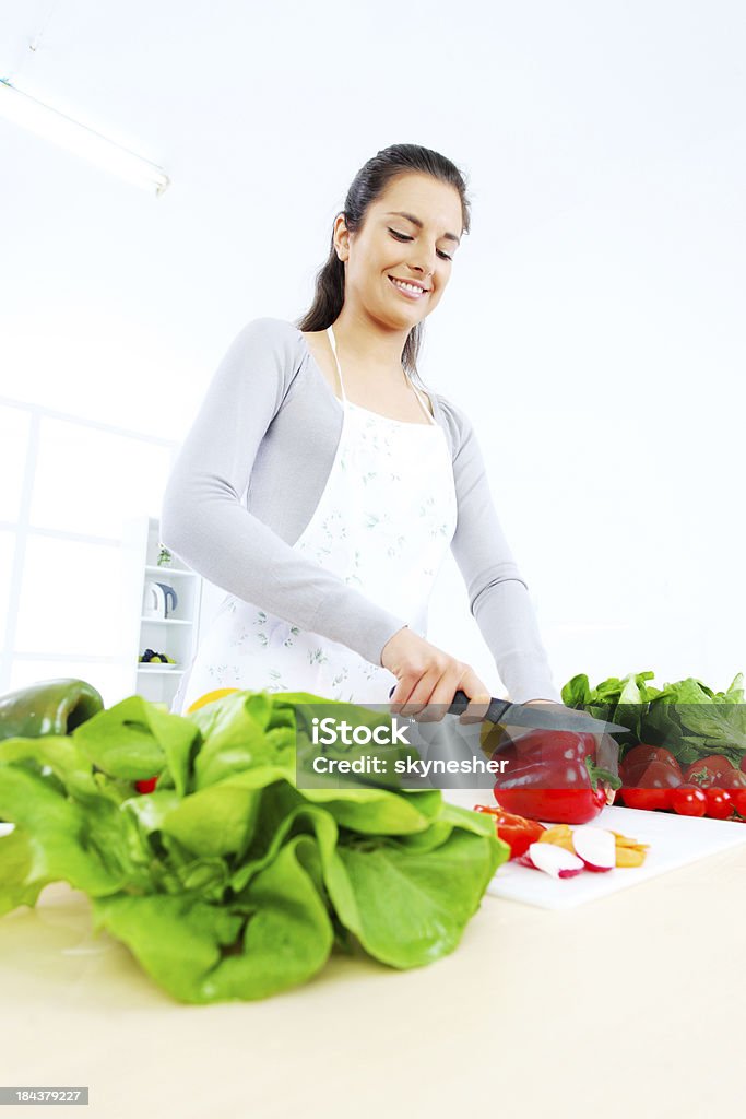 Smiling young woman making salad in the kitchen. Young woman preparing salad. White background. White Background Stock Photo