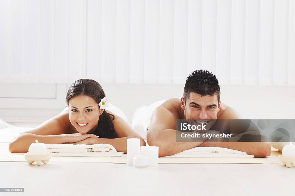 Young couple is resting at the spa centre. Front view of a beautiful love couple lying on the towels at the spa centre. White background. Adult Stock Photo