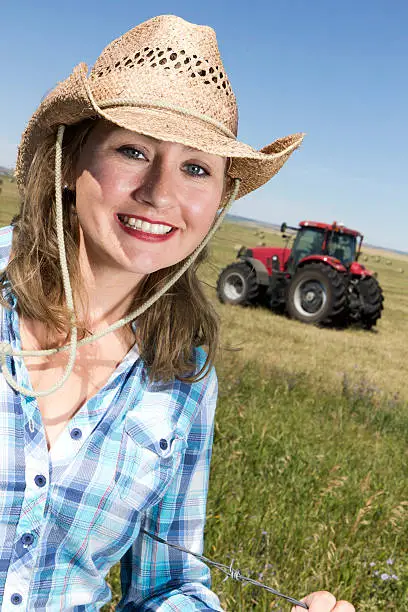 An image from the farming industry of a female farmer in a field a tractor behind her.