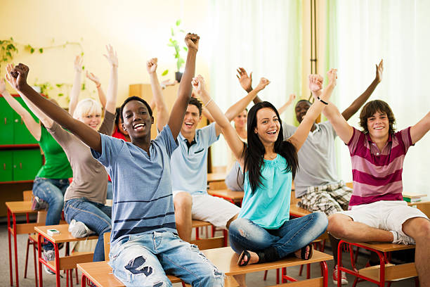 istock Large group of students sitting on desks with raised arms. 184383076