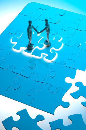 Business agreement concept with wooden figures shaking hands on a jigsaw puzzle