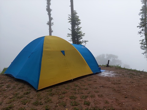 Foggy weather view with yellow and blue tent for camping on the mountain