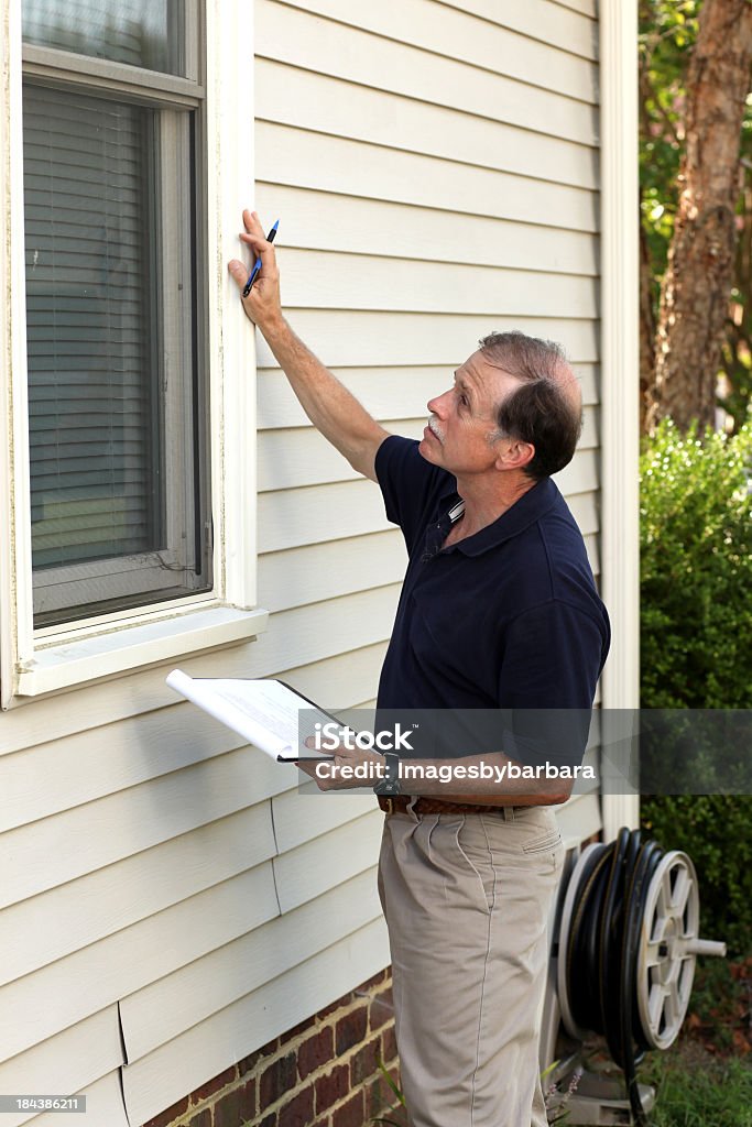 Home inspector examining the window outside of a white house Inspector checking windows of home. Building Contractor Stock Photo