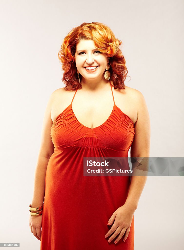 Voluptuoso sonriente mujer de pelo roja usando vestido rojo - Foto de stock de 20 a 29 años libre de derechos