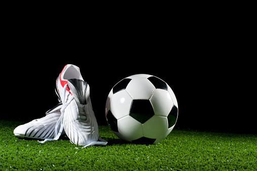 Soccer ball and boots on grass at night