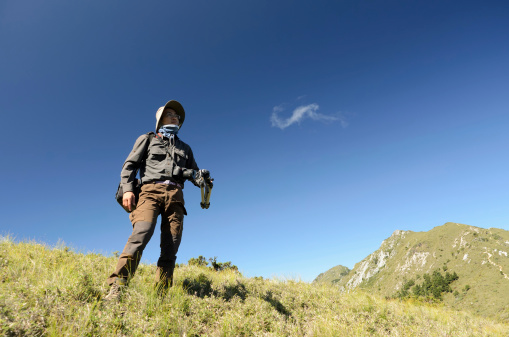 Outdoor photographer man standing on grassland of mountain under blue sky.