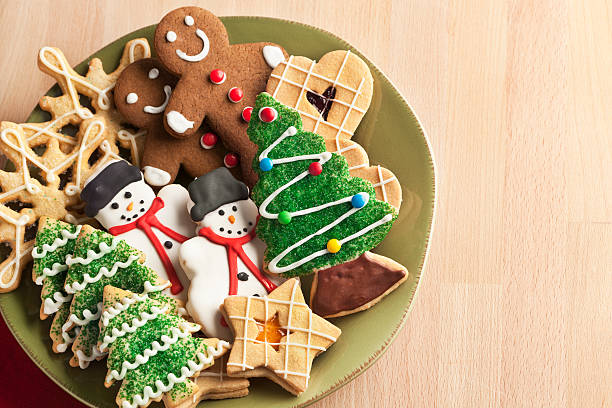 Christmas Cookie Holiday Plate Featuring Tree, Gingerbread, Snowman, Snowflake Desserts A plate filled with Christmas cookies decorated with frosting and icing for winter holiday celebrations. The baked dessert collection of sweet food features Christmas tree, gingerbread man, snowman, star, heart, and snowflake shapes against the green background of a ceramic plate. The light wooden table area allows for copy space. cookie stock pictures, royalty-free photos & images