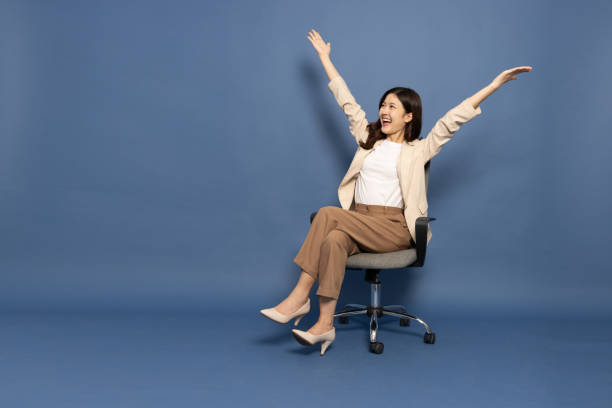 attraktive schöne asiatische frau sitzt auf bürostuhl und hebt die arme vor glück, aufgeregte geschäftsfrau gewinner-erfolgskonzept - office chair cheering ecstatic success stock-fotos und bilder