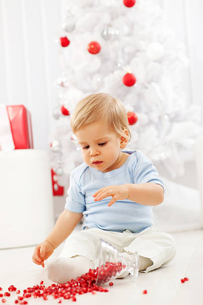 Little boy on New Years day eating pomegranate. Beautiful baby boy sitting and playing with the pomegranate that he spilt on the floor. baby new years eve new years day new year stock pictures, royalty-free photos & images