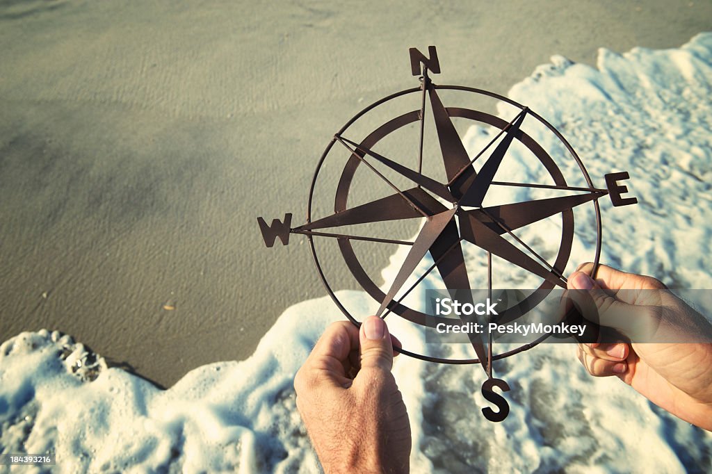 Hands Holding Compass Over Waves Rushing on Beach Hands hold rusty old compass over smooth sand with waves rushing ashore on beach Spirituality Stock Photo