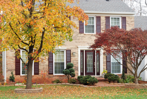 A two story suburban home in autumn with a maple tree in front yard and fallen leaves on lawn.