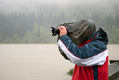 Photographer taking pfoto in the rain. The camera is protected by cover and his head is under plastic bag.