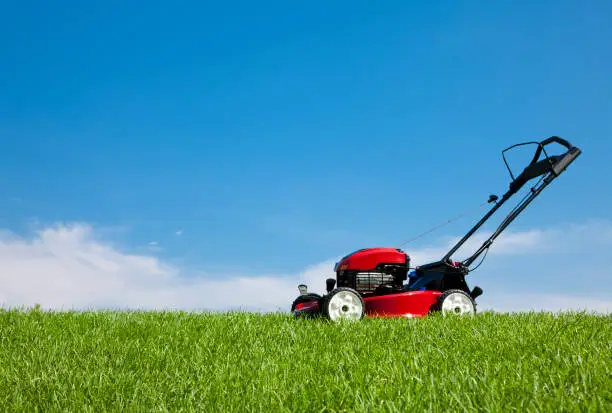 Lawn mower on lush green grass on a summer day under a blue sky.