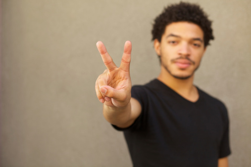 A young man makes the symbol of a peace sign with two fingers. Shallow depth of field. Selective focus on fingers.