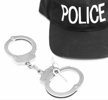 A police cap and steel authentic handcuffs on white background.