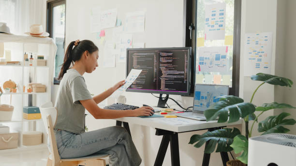 Side view of professional young Asia girl IT development programmer typing on keyboard coding programming fixing data code on computer screen and laptop on table in workroom at house office. programador profesional de desarrollo de ti joven de asia que escribe en la programación de codificación del teclado que fija el código de datos en la pantalla de la computadora y la computadora portátil en la mesa en la sala de trabajo de la oficina d
